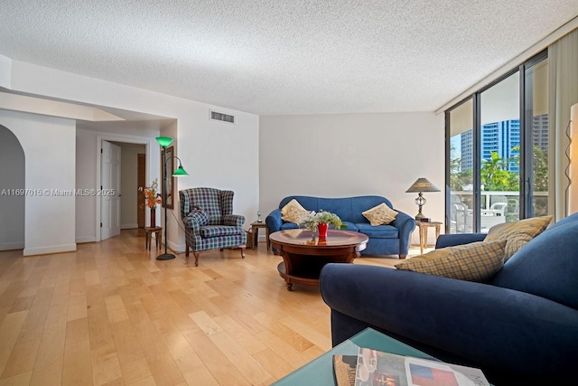 living room featuring visible vents, a textured ceiling, light wood-type flooring, and a wall of windows