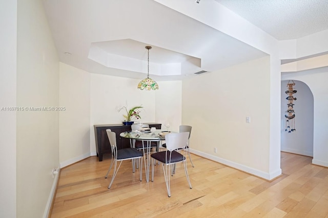 dining area with a tray ceiling, wood finished floors, visible vents, and baseboards