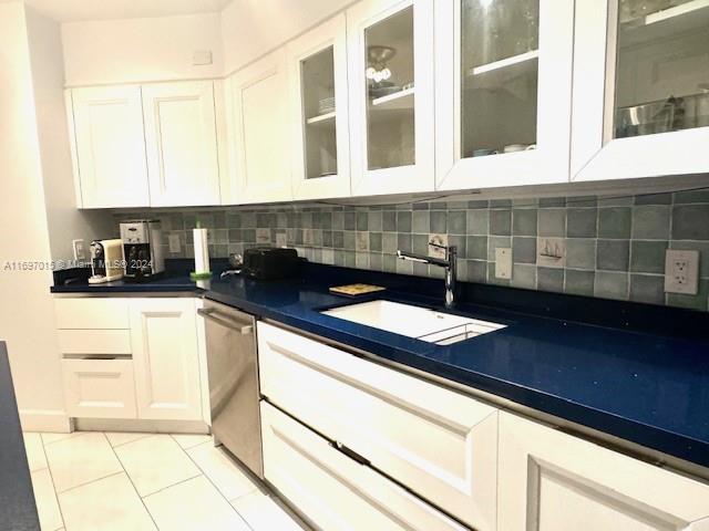 kitchen with sink, white cabinets, stainless steel dishwasher, decorative backsplash, and light tile patterned flooring