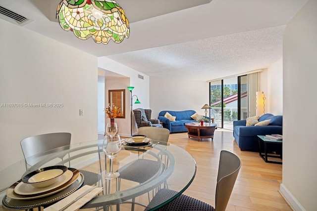 dining room featuring visible vents, baseboards, expansive windows, light wood-style flooring, and a textured ceiling