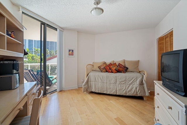 bedroom with expansive windows, a textured ceiling, light wood finished floors, baseboards, and access to exterior