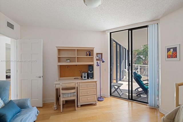 office space featuring visible vents, light wood-style floors, floor to ceiling windows, and a textured ceiling