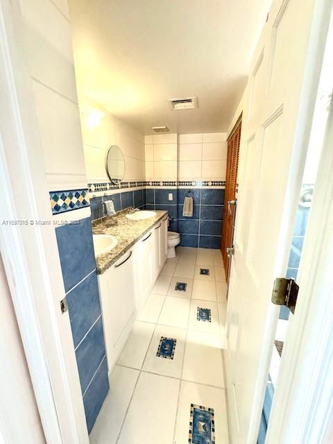 bathroom featuring tile patterned flooring, vanity, toilet, and tile walls