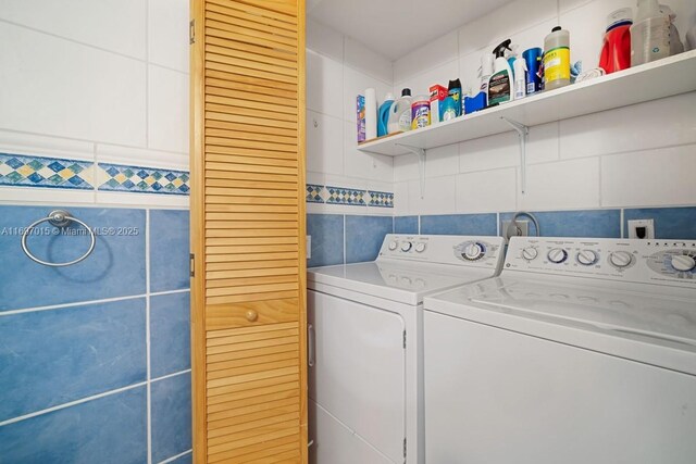 clothes washing area featuring washing machine and clothes dryer, laundry area, and tile walls