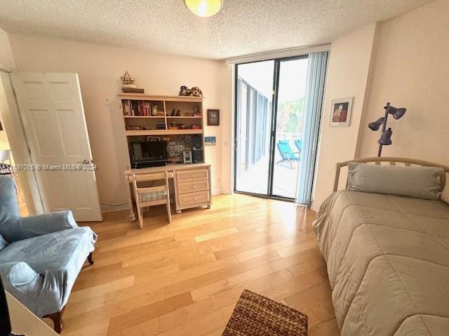 bedroom with access to exterior, light hardwood / wood-style flooring, a textured ceiling, and a wall of windows