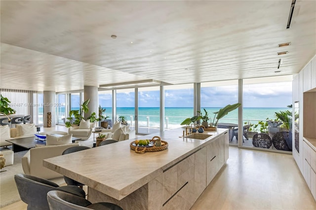 kitchen with light wood-type flooring, a view of the beach, a water view, a wall of windows, and a center island