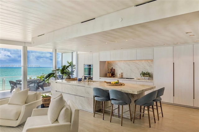 kitchen featuring a kitchen bar, a water view, white cabinetry, and light hardwood / wood-style floors