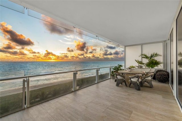 balcony at dusk featuring a water view and a view of the beach