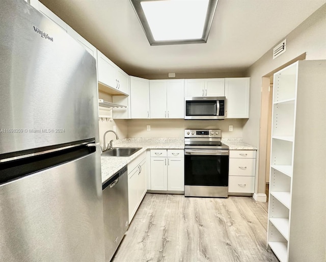 kitchen with light stone countertops, sink, stainless steel appliances, white cabinets, and light wood-type flooring