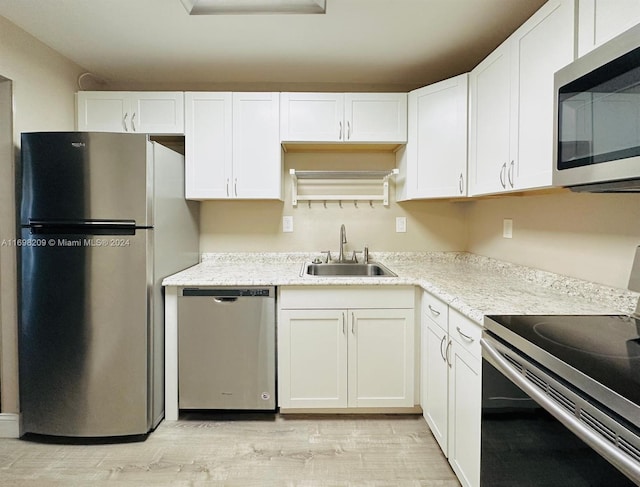 kitchen with light stone countertops, stainless steel appliances, sink, white cabinets, and light hardwood / wood-style floors