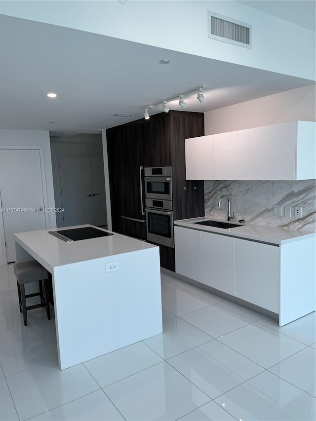 kitchen with a center island, sink, stainless steel double oven, tasteful backsplash, and white cabinets