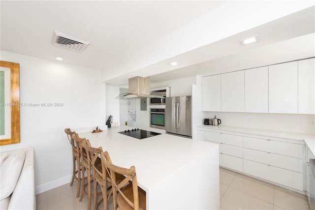 kitchen featuring kitchen peninsula, appliances with stainless steel finishes, a breakfast bar, white cabinets, and light tile patterned flooring