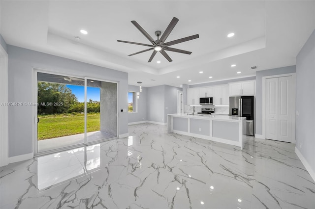 unfurnished living room featuring ceiling fan, plenty of natural light, a tray ceiling, and sink