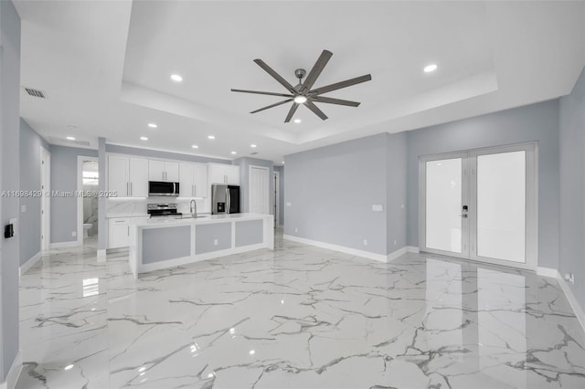 unfurnished living room featuring a raised ceiling, ceiling fan, and sink