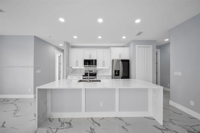 kitchen featuring stainless steel appliances, white cabinets, a large island, and light stone countertops