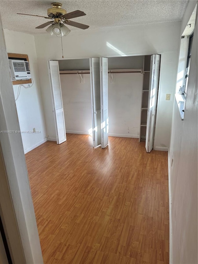 unfurnished bedroom with a textured ceiling, ceiling fan, light hardwood / wood-style flooring, and two closets