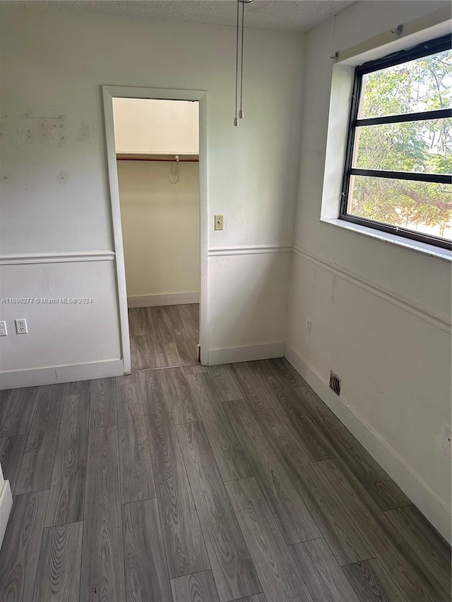 unfurnished bedroom featuring a textured ceiling, a spacious closet, dark wood-type flooring, and a closet