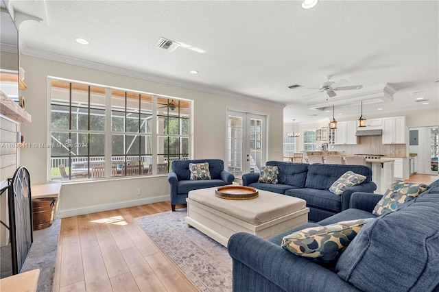 living room featuring a textured ceiling, light wood-type flooring, ceiling fan, and crown molding