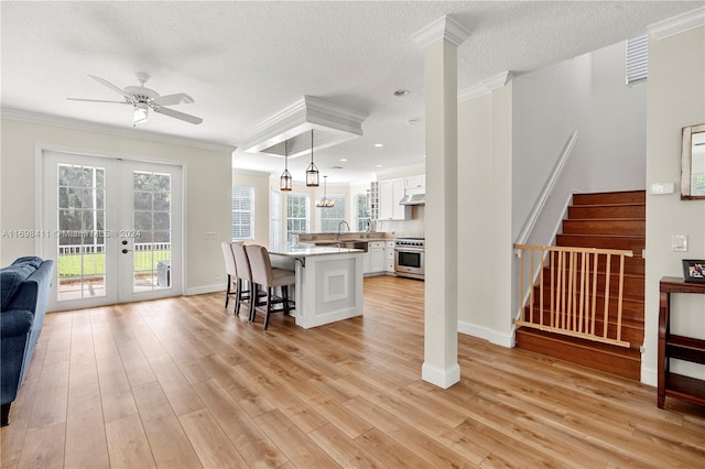 interior space featuring a kitchen bar, light wood-type flooring, white cabinets, stainless steel stove, and hanging light fixtures