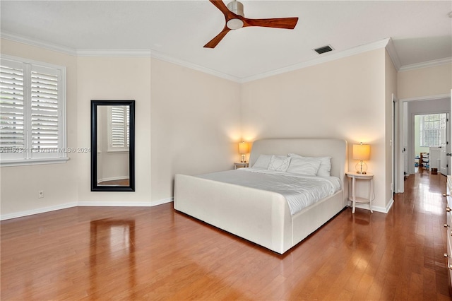 bedroom featuring multiple windows, hardwood / wood-style floors, ceiling fan, and ornamental molding