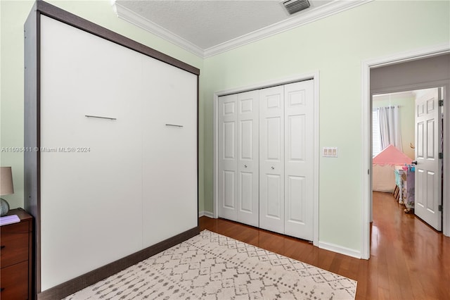 bedroom with hardwood / wood-style floors, crown molding, a textured ceiling, and a closet