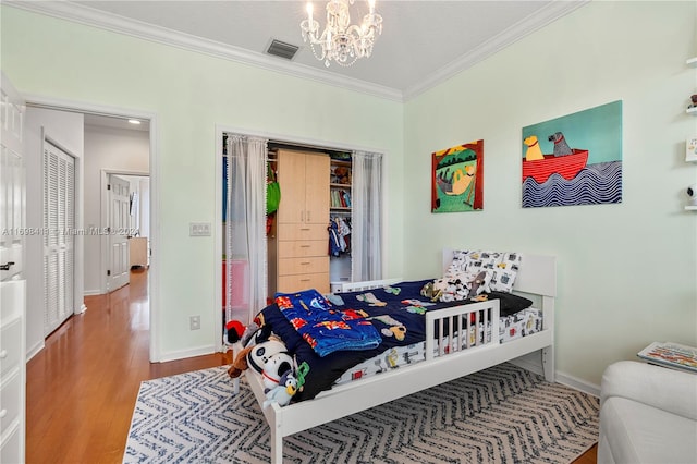 bedroom with a closet, wood-type flooring, ornamental molding, and a chandelier