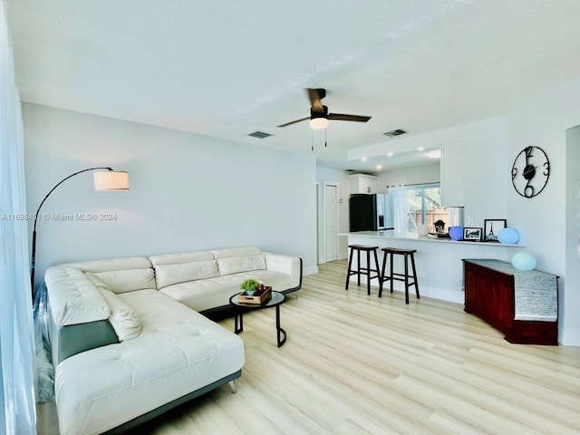 living room with ceiling fan, light hardwood / wood-style flooring, and a textured ceiling