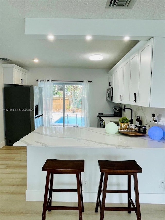 kitchen with white cabinets, a kitchen breakfast bar, kitchen peninsula, and appliances with stainless steel finishes