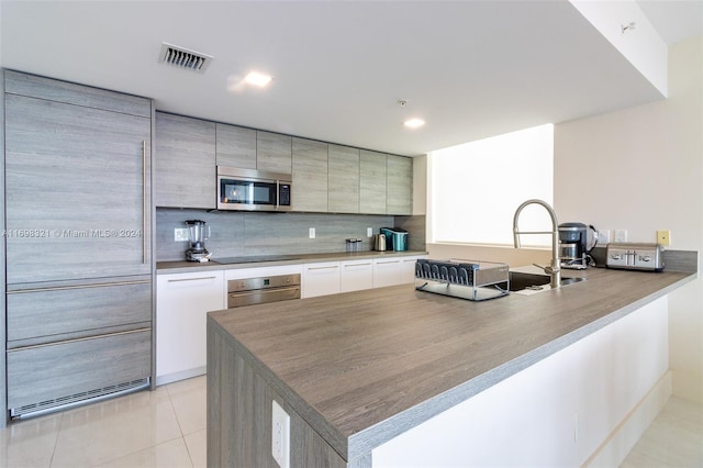 kitchen featuring kitchen peninsula, appliances with stainless steel finishes, backsplash, sink, and light tile patterned floors