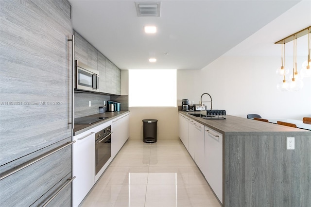 kitchen featuring white cabinetry, sink, hanging light fixtures, light tile patterned flooring, and appliances with stainless steel finishes