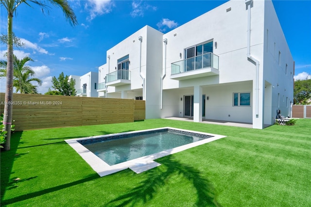 rear view of property with a fenced in pool, a balcony, a lawn, and a patio