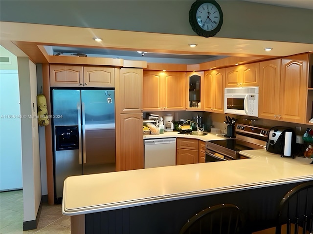 kitchen featuring kitchen peninsula, appliances with stainless steel finishes, a kitchen breakfast bar, light brown cabinets, and light tile patterned floors