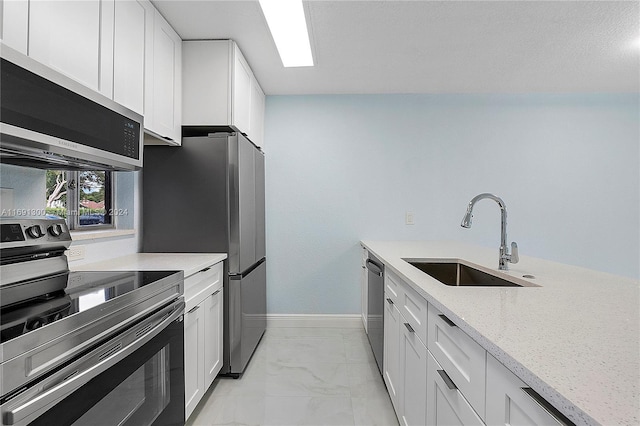 kitchen with light stone countertops, sink, white cabinets, and stainless steel appliances