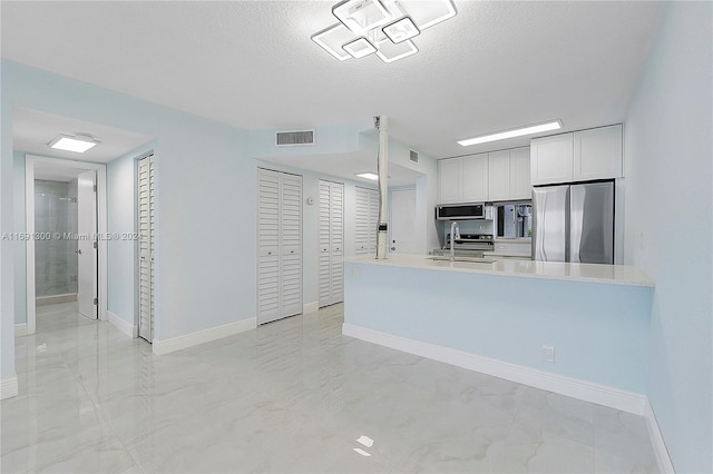 kitchen featuring kitchen peninsula, white cabinetry, a textured ceiling, and appliances with stainless steel finishes