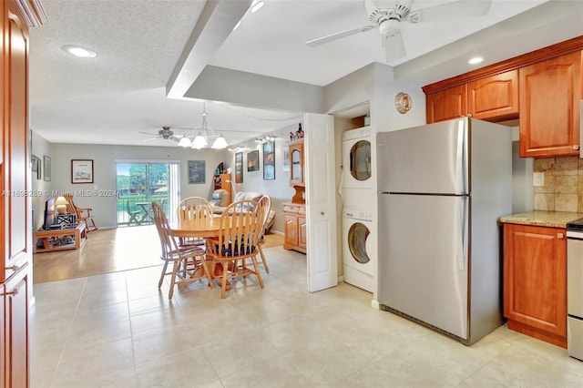 kitchen with backsplash, ceiling fan with notable chandelier, stainless steel fridge, a textured ceiling, and stacked washer / drying machine