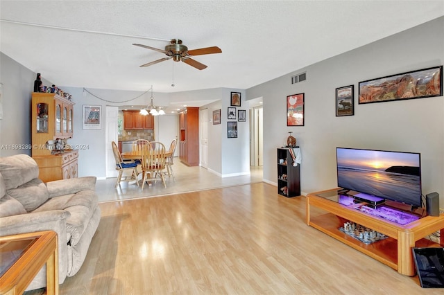 living room featuring ceiling fan with notable chandelier, light hardwood / wood-style floors, and a textured ceiling