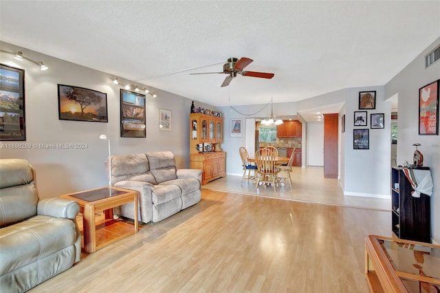 living room with ceiling fan with notable chandelier, light hardwood / wood-style floors, and a textured ceiling