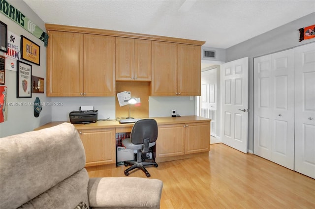 home office featuring a textured ceiling, built in desk, and light hardwood / wood-style flooring