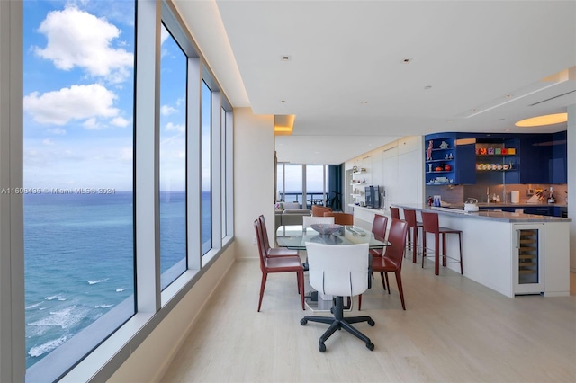 dining space featuring bar area, a water view, wine cooler, and light hardwood / wood-style floors