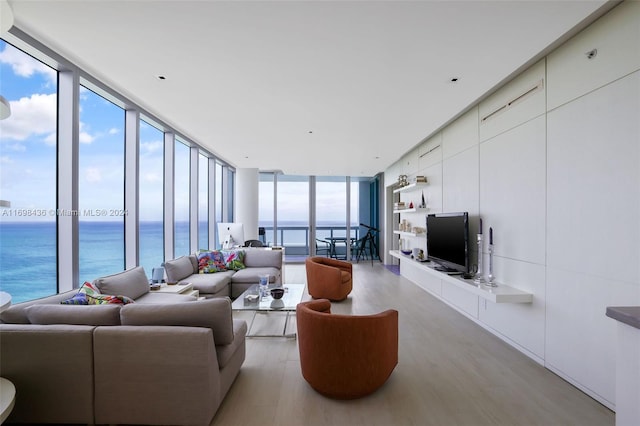 living room with floor to ceiling windows, a water view, and light hardwood / wood-style flooring