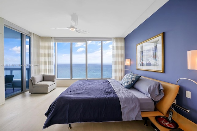 bedroom with light wood-type flooring, a water view, expansive windows, and ceiling fan