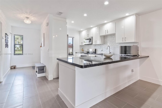 kitchen with dark stone counters, kitchen peninsula, appliances with stainless steel finishes, tasteful backsplash, and white cabinetry