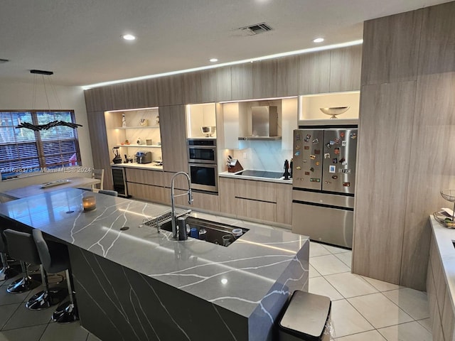 kitchen with a large island, sink, wall chimney exhaust hood, light tile patterned floors, and appliances with stainless steel finishes