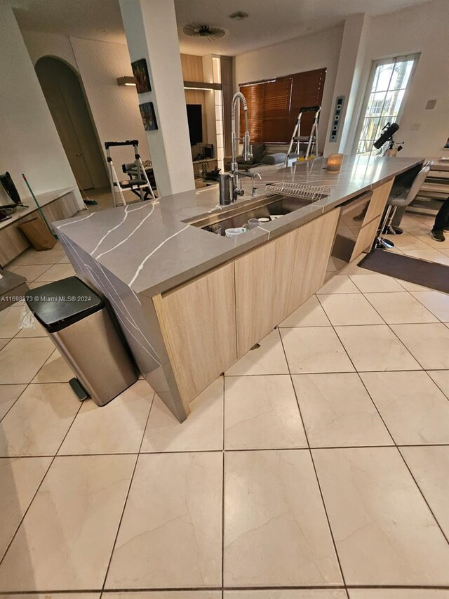 kitchen featuring light tile patterned flooring, light brown cabinets, stainless steel dishwasher, and sink