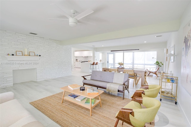 living room featuring ceiling fan, brick wall, and light wood-type flooring