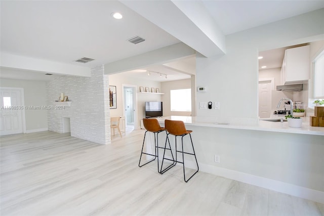 kitchen with white cabinetry, kitchen peninsula, plenty of natural light, light hardwood / wood-style floors, and a breakfast bar area