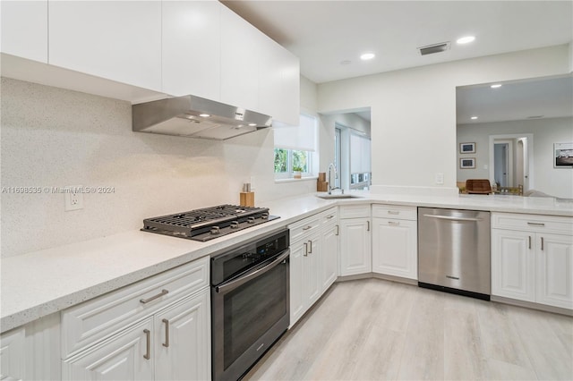 kitchen with sink, appliances with stainless steel finishes, white cabinets, exhaust hood, and light wood-type flooring