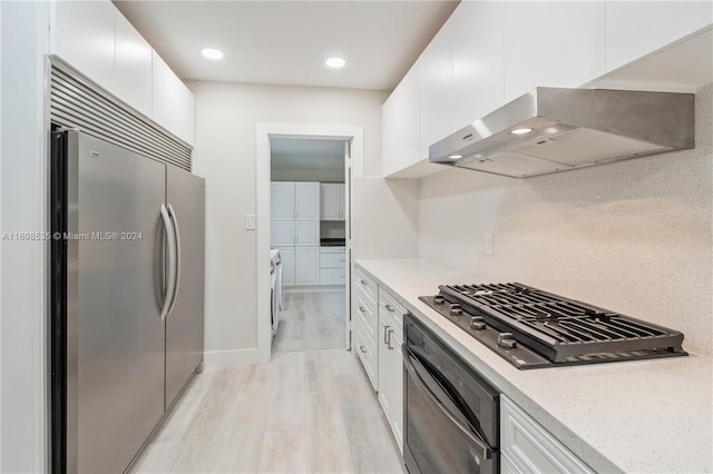 kitchen with white cabinetry, wall chimney exhaust hood, stainless steel appliances, light hardwood / wood-style floors, and decorative backsplash