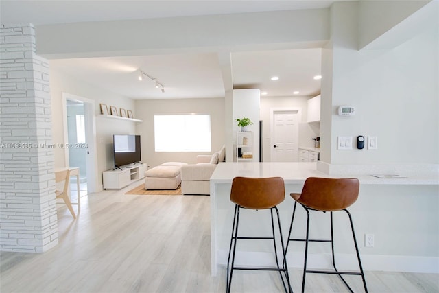 kitchen featuring a kitchen bar, kitchen peninsula, white cabinetry, and light wood-type flooring