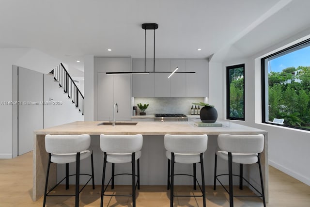 kitchen with a kitchen bar, tasteful backsplash, sink, pendant lighting, and light hardwood / wood-style floors